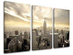 Třídílný obraz na plátně zachycuje panoramatický pohled na New York s mrakodrapy a zataženou oblohou ve zlatavých tónech, Papilora.