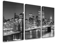 Třídílný černobílý obraz na plátně zachycuje noční panorama New Yorku s osvětleným Brooklynským mostem a mrakodrapy, viditelný je dřevěný rám Papilora.