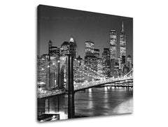 Černobílý tisk na plátně zachycuje noční panorama New Yorku s Brooklynským mostem a osvětlenými mrakodrapy, viditelný je dřevěný rám Papilora.