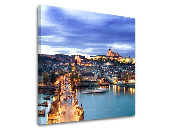 Na plátně je zachycen noční pohled na Karlův most a Pražský hrad v modrých a zlatých tónech, s viditelným dřevěným rámem Papilora.
