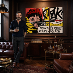 Pop-artový obraz ženy s puškou a komiksovými nápisy v červené, žluté a černé barvě visí v moderním interiéru nad dřevěnou konzolí s vázou a svíčkou Papilora.