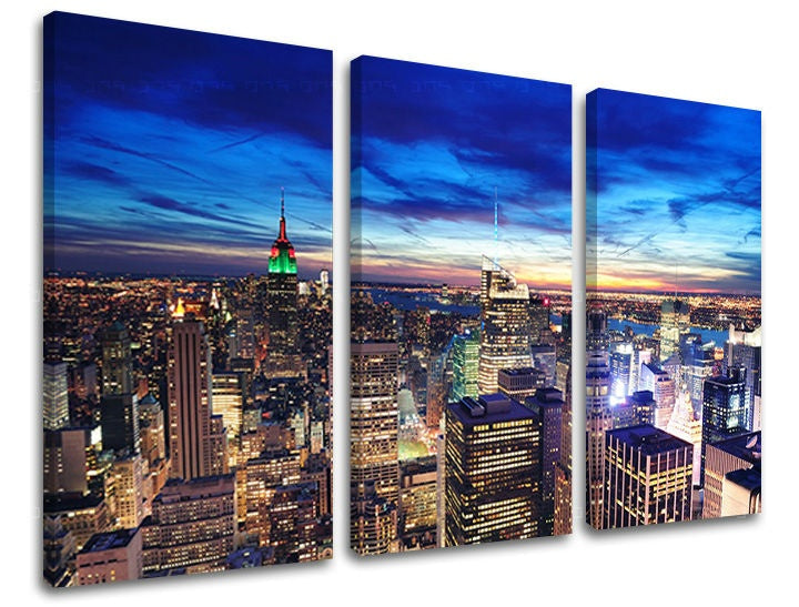 Třídílný obraz na plátně zachycuje noční panorama New Yorku s rozsvícenými mrakodrapy a modrou oblohou, viditelný je i dřevěný rám Papilora.