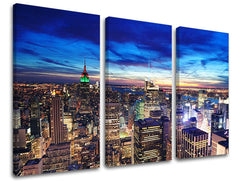 Třídílný obraz na plátně zachycuje noční panorama New Yorku s rozsvícenými mrakodrapy a modrou oblohou, viditelný je i dřevěný rám Papilora.