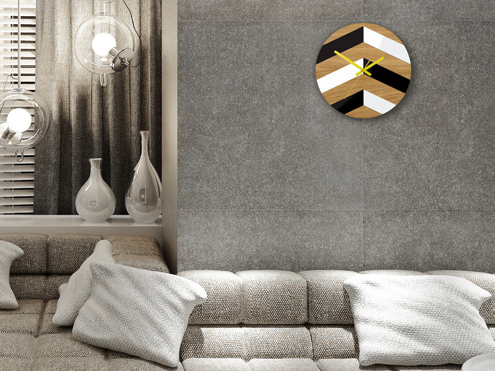 Moderní nástěnné hodiny s geometrickým vzorem v černé, bílé a dřevěné barvě se žlutými ručičkami visí v elegantním interiéru nad dřevěnou konzolí s vázou a svíčkou Papilora.