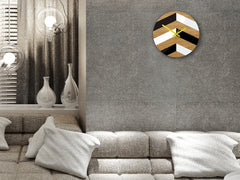 Moderní nástěnné hodiny s geometrickým vzorem v černé, bílé a dřevěné barvě se žlutými ručičkami visí v elegantním interiéru nad dřevěnou konzolí s vázou a svíčkou Papilora.