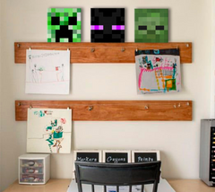 Tři čtvercové obrazy s pixelovými hlavami postav ze hry Minecraft, včetně zeleného Creepera, jsou zavěšeny nad dětskou postelí s hračkami, Papilora.