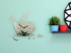 Nástěnné hodiny ve tvaru šálku kávy s nápisem 'Coffee Time' a zrnky kávy, v lesklém stříbrném provedení, visí v moderním stylovém interiéru nad dřevěnou konzolí s vázou a svíčkou Papilora.