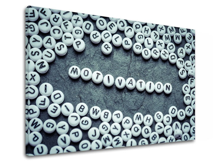 Přiblížený detail slova MOTIVATION vytvořeného z bílých korálků s černými písmeny, obklopeného dalšími korálky Papilora.