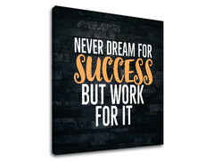 Plátno s motivačním citátem „NEVER DREAM FOR SUCCESS BUT WORK FOR IT“ v bílé a oranžové barvě na tmavém pozadí, s viditelným dřevěným rámem Papilora.