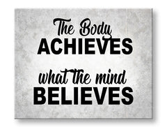 Obraz s motivačním citátem „The Body Achieves What The Mind Believes“ visí v moderním interiéru nad dřevěnou konzolí s vázou a svíčkou Papilora.