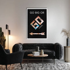 Obraz s nápisem „GO BIG OR GO HOME“ a šipkou visí v moderním interiéru nad dřevěnou konzolí s vázou a svíčkou Papilora.