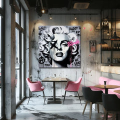 Obraz s portrétem Marilyn Monroe v pop-art stylu, s černými a růžovými detaily na šedém pozadí, visí v moderním interiéru nad dřevěnou konzolí s vázou a svíčkou Papilora.