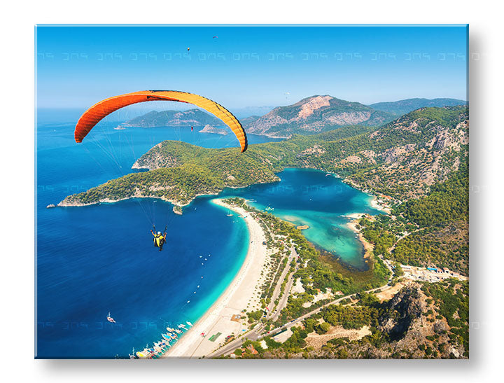 Obraz s paraglidingem nad modrou lagunou visí v moderním interiéru nad dřevěnou konzolí s vázou a svíčkou Papilora.