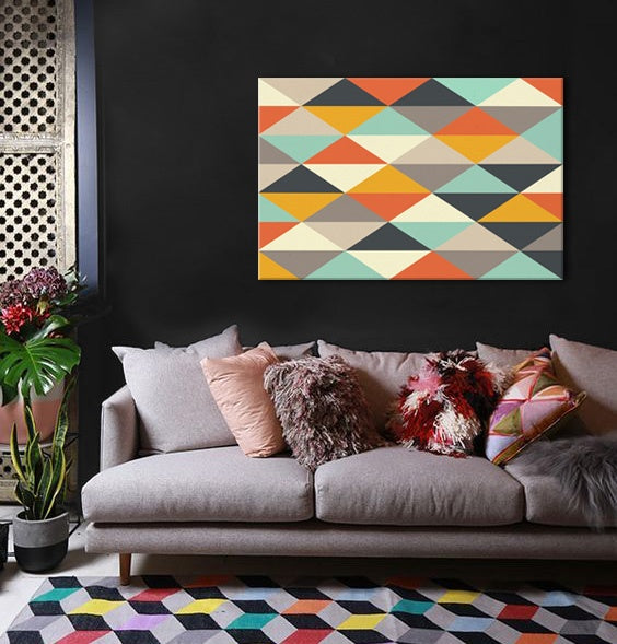 Moderní obraz s geometrickým vzorem trojúhelníků v oranžových a tyrkysových tónech visící nad šedou pohovkou v elegantním interiéru Papilora.