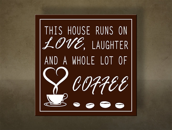 Hnědý obraz s bílým nápisem „THIS HOUSE RUNS ON LOVE, LAUGHTER AND A WHOLE LOT OF COFFEE“ a šálkem kávy s kávovými zrny, viditelný na dřevěném rámu Papilora.