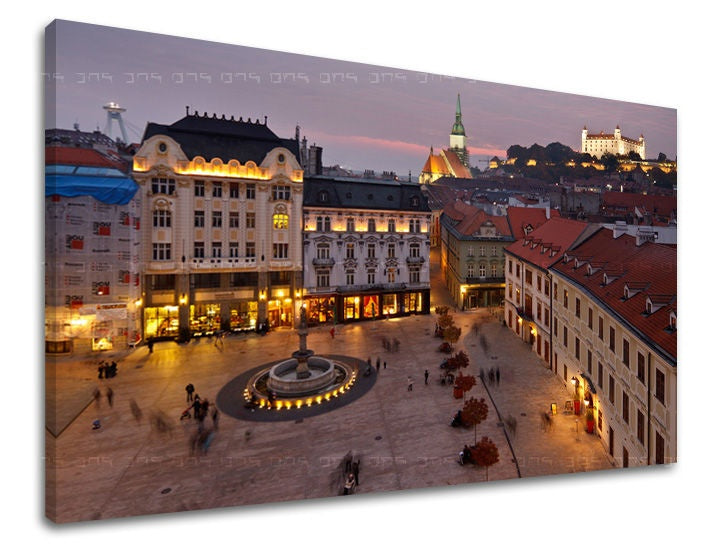 Na plátně je zachyceno večerní panorama Bratislavy s osvětleným náměstím a hradem v pozadí, v teplých odstínech fialové a žluté, Papilora.
