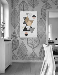 Abstraktní obraz s geometrickými tvary v šedé, černé a zlaté barvě visí v moderním interiéru nad dřevěnou konzolí s vázou a svíčkou Papilora.