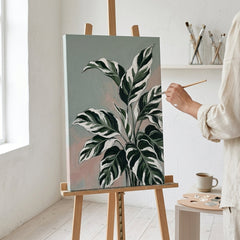 Umělec v ateliéru Papilora pracuje na dokončení detailů obrazu s tropickými listy, přirozené světlo dopadající na plátno.