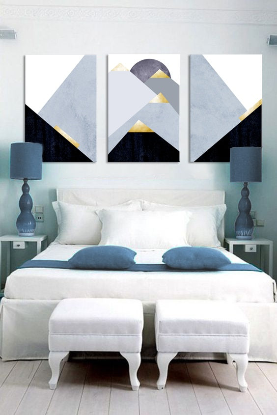 Abstraktní triptych s horami v modrých a zlatých tónech visí nad dřevěnou konzolí s vázou a svíčkou v moderním interiéru Papilora.