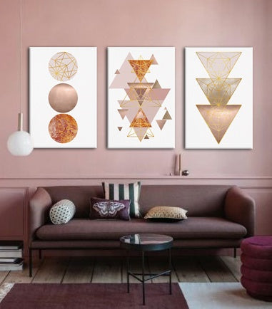 Moderní interiér s růžovou stěnou, nad hnědou pohovkou visí tři plátna s geometrickými tvary, doplňuje je váza a svíčka na konzoli Papilora.