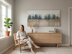 Ručně malovaný obraz STROMY 140x70 cm na plátně, zavěšený v moderním obývacím pokoji. Bílo-modré tóny, hory a stromy, evokuje klid a přírodu.